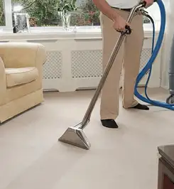 Professional carpet cleaner using a hot-water extraction wand and hose machine in a living room in Chandler, AZ.