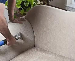 Professional upholstery cleaner deep-cleaning a fabric sofa with a handheld extraction tool and hose in Chandler, AZ.